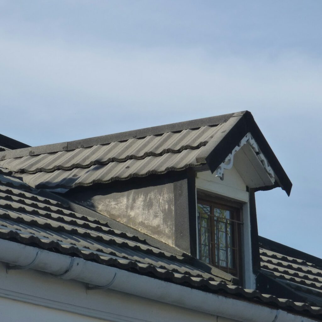 Snow rests on a durable residential roof with metal panels, slate sections, and carefully sealed flashing around a chimney.