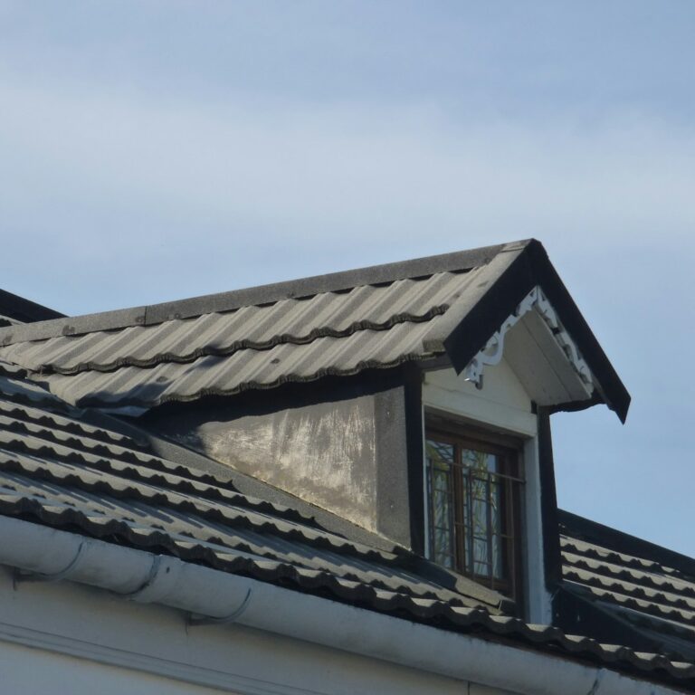 Snow rests on a durable residential roof with metal panels, slate sections, and carefully sealed flashing around a chimney.